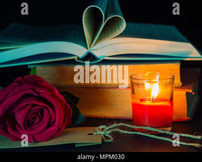 Tasto basso di San Valentino di background-red rose con candela rossa e il libro aperto a forma di cuore sulla pila di libri. Foto Stock