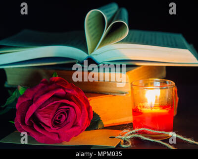 Tasto basso di San Valentino di background-red rose con candela rossa e il libro aperto a forma di cuore sulla pila di libri. Foto Stock