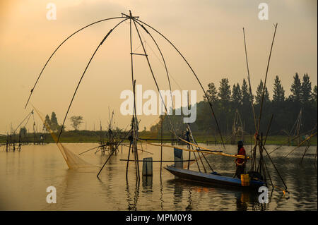 Udonthani, Thailandia - Dicembre 9, 2011: pescatore sulla barca da pesca con tradizionali net strumenti da pesca nella palude durante il tramonto Foto Stock