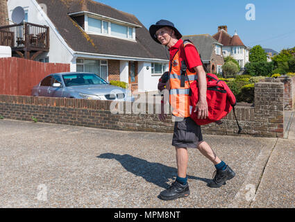 British portalettere che indossano pantaloncini camminando in una zona residenziale che trasportano un rosso sacchetta di lettere, per le consegne di mattina nel West Sussex, in Inghilterra, Regno Unito. Foto Stock