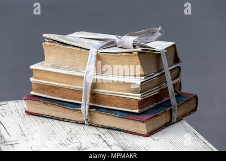 Pila di libri usurati legato con il vecchio nastro bianco su una tavola di legno al di fuori su sfondo grigio. Foto Stock