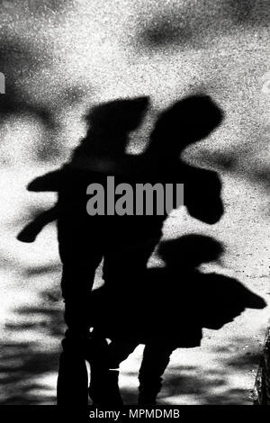 Sfocata ombra silhouette di una famiglia , padre trasporta un bambino toddler sui fianchi , figlia camminando dietro di loro , in bianco e nero Foto Stock