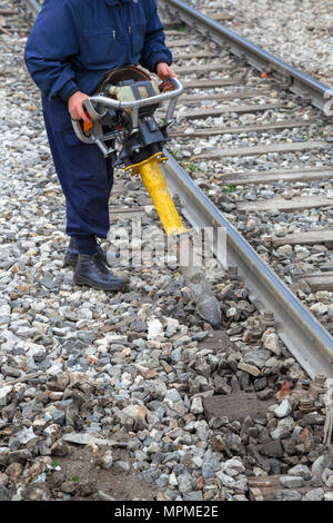 Lavoratore di eseguire le operazioni di manutenzione della strada sui binari della ferrovia tramite vibrazione verticale tamper. Foto Stock