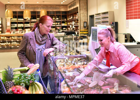 Giovane commessa al contatore di fresco nel supermercato - vendita di formaggi e carni Foto Stock