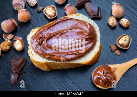 Fetta di pane con il diffondersi di crema di cioccolato e nocciole sulla tavola nera. Serve una deliziosa colazione concetto. Foto Stock