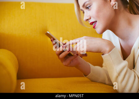 Donna bionda sdraiato sul divano, utilizza lo smartphone a casa Foto Stock