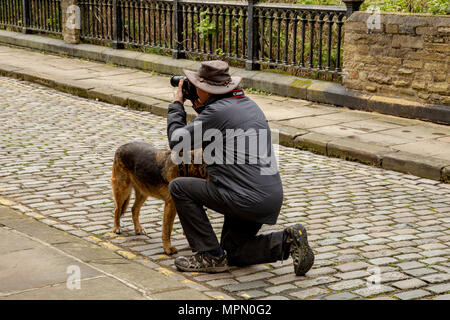 Un uomo si inginocchia per scattare una fotografia in Saltair, Yorkshire. Il suo cane sorge accanto a lui. Foto Stock