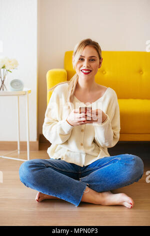 Donna bionda utilizza lo smartphone a casa Foto Stock
