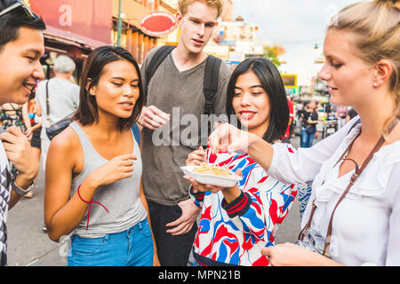 Thailandia, Bangkok, Khao San Road, gruppo di amici degustazione di cibo locale sulla strada del mercato Foto Stock