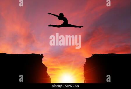 Silhouette di una ragazza ballerino in uno split leap su scogli pericolosi con drammatico tramonto o l'alba di sfondo e copiare lo spazio. Concetto di fede, conquerin Foto Stock