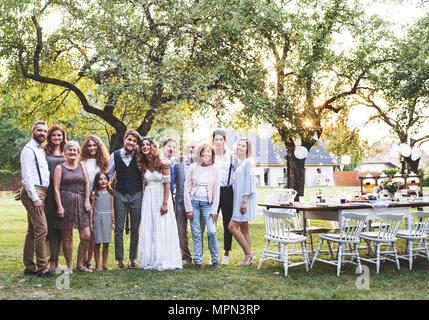 Sposa e lo sposo, gli ospiti che posano per una foto al ricevimento di nozze al di fuori nel cortile. Foto Stock