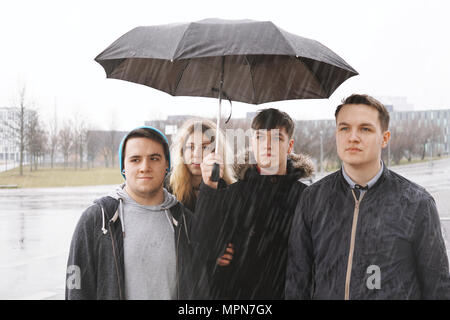 Un gruppo di giovani adolescenti urbano amici sotto un unico ombrello sotto la pioggia Foto Stock