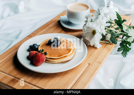 La prima colazione a letto con frittelle e caffè sul vassoio in legno Foto Stock