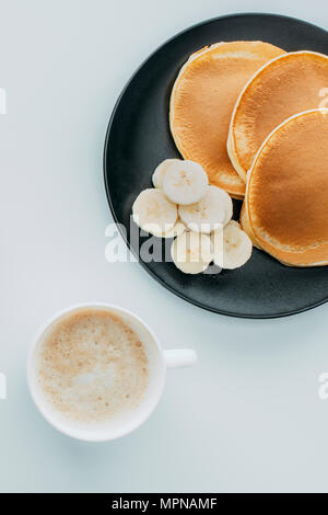 Vista superiore del pancake con fette di banana e la tazza di caffè sul tavolo bianco Foto Stock