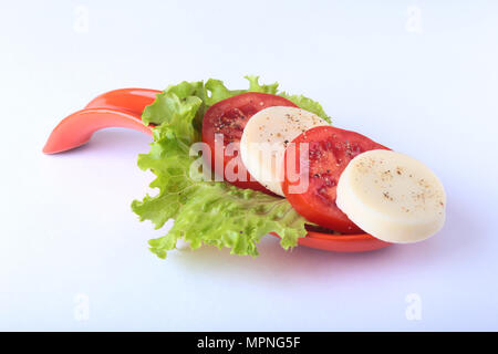 Porzione di mozzarella con pomodori, foglia di lattuga e condimento balsamico su red portionen piastra. isolato su bianco. messa a fuoco selettiva di close-up shot. Foto Stock