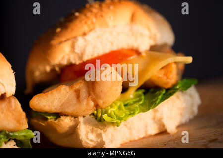 Un filetto di merluzzo giallo, Pollachius pollachius, che è stata rivestita in farina e fritte, servita su un burger panino con lattuga, pomodoro grigliate e fondere Foto Stock