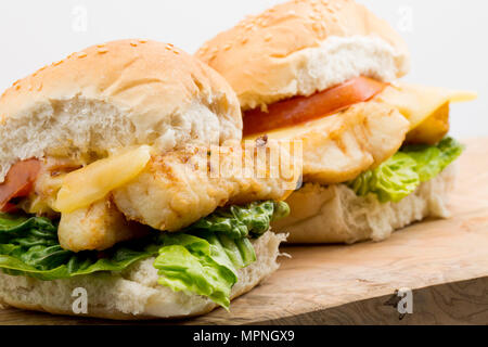 Un filetto di merluzzo giallo, Pollachius pollachius, che è stata rivestita in farina e fritte, servita su un burger panino con lattuga, pomodoro grigliate e fondere Foto Stock