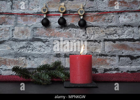 Candela che brucia e decorazione di Natale di fronte a un muro di mattoni Foto Stock