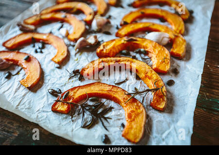 Cotta fette di zucca, aglio e rosmarino sulla carta da forno Foto Stock