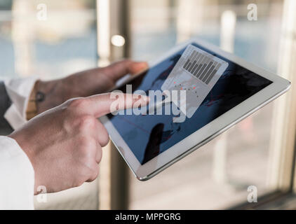 Donna che utilizza tablet in ufficio con dati emergenti dalla schermata Foto Stock