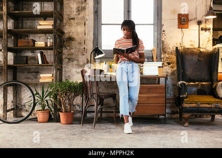 Giovane donna in piedi nella parte anteriore della scrivania in un loft utilizzando notebook Foto Stock