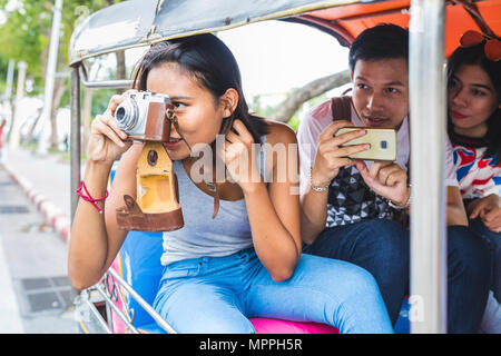 Thailandia, Bangkok, tre amici in sella tuk tuk a scattare foto con lo smartphone Foto Stock