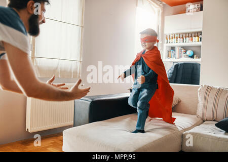 Padre giocando con il suo piccolo figlio vestito come un supereroe a casa Foto Stock