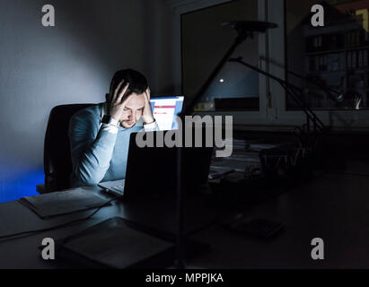 Imprenditore stanco seduto alla scrivania in ufficio durante la notte Foto Stock