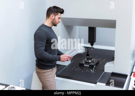 Uomo con carta di esaminare la macchina nel moderno stabilimento Foto Stock