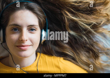 Ritratto di sorridente giovane donna con cuffie giacente sul letto Foto Stock