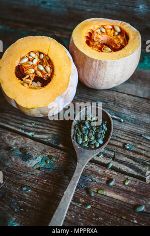 Due metà di una zucca e un cucchiaio di semi di zucca su legno Foto Stock