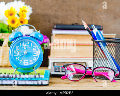 Accessori per ufficio compreso stack del libro, calcolatrice, bicchieri, matita rossa, penna blu,sveglia e fiore rosa su sfondo di legno. Istruzione e Foto Stock