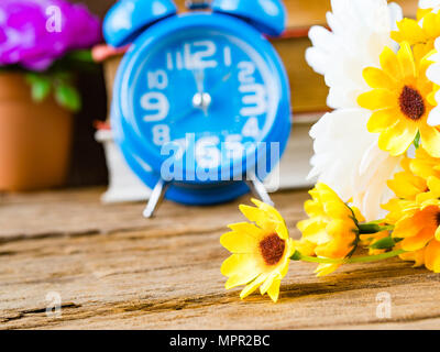 Accessori per ufficio compreso stack del libro, sveglia e rosa e giallo fiore bianco su sfondo di legno. L'istruzione e la concezione di business. Foto Stock