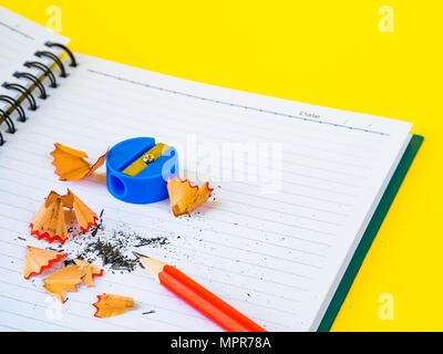 Accessori per ufficio tra cui note book, matita rossa e blu sharpener su sfondo giallo. L'istruzione e la concezione di business. Foto Stock