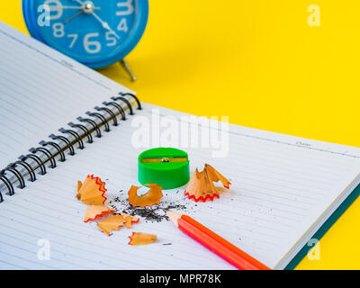 Accessori per ufficio tra cui note book, matita rossa, sveglia e affilatrice verdi su sfondo giallo. L'istruzione e la concezione di business. Foto Stock