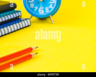 Accessori per ufficio tra cui nota libri, matita rossa e sveglia su sfondo giallo. L'istruzione e la concezione di business. Foto Stock