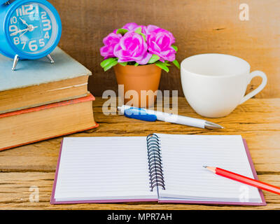 Accessori per ufficio tra cui note book, matita rossa, sveglia e fiore su sfondo di legno. L'istruzione e la concezione di business. Foto Stock