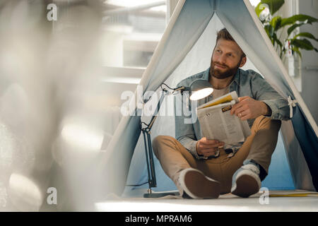 L'uomo camping nel suo salotto, leggendo il giornale Foto Stock