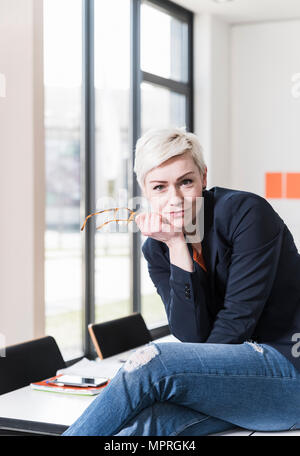 Ritratto di fiducioso imprenditrice seduta sul tavolo in ufficio Foto Stock