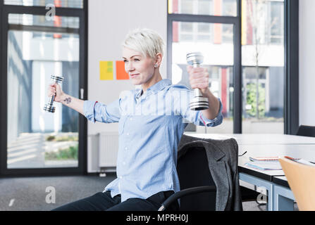 Donna sorridente esercizio con manubri in office Foto Stock