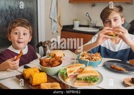 Due ragazzi con il cane gustando piatti americani al tavolo da pranzo a casa Foto Stock