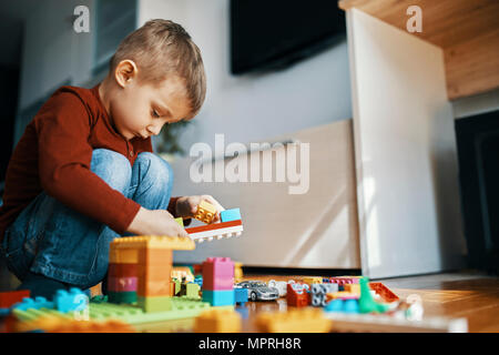 Bambino accovacciato sul pavimento a casa giocando con mattoni da costruzione Foto Stock