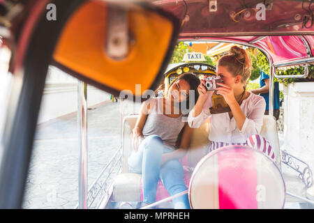 Thailandia, Bangkok, due amici a cavallo tuk tuk a scattare foto con una vecchia macchina fotografica Foto Stock