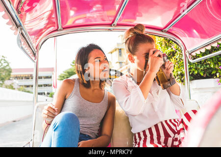 Thailandia, Bangkok, due amici a cavallo tuk tuk a scattare foto con una vecchia macchina fotografica Foto Stock