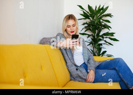 Imprenditrice seduta sul divano giallo, utilizza lo smartphone Foto Stock