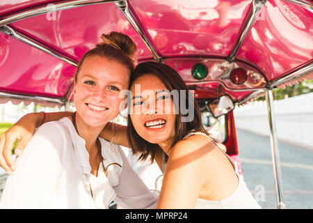 Thailandia, Bangkok, ritratto di due felici due amici equitazione tuk tuk Foto Stock