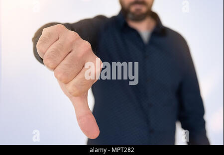 Imprenditore in maglietta blu che mostra il pollice verso il basso gesto Foto Stock
