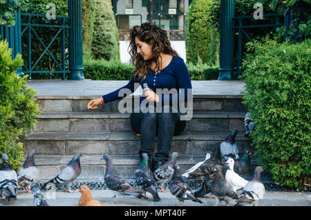 Bella donna sorridente alimentare piccioni in il parco durante la giornata al parco di amicizia in Surco, Lima - Perù Foto Stock