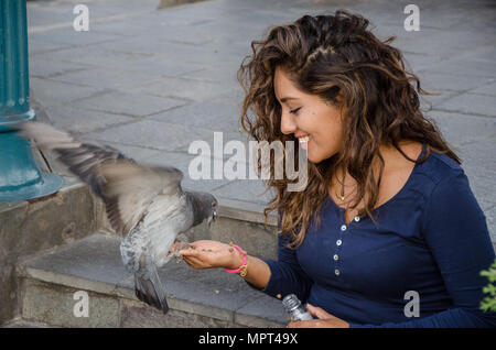 Donna sorridente alimentando un piccione dalla sua mano nel parco Foto Stock