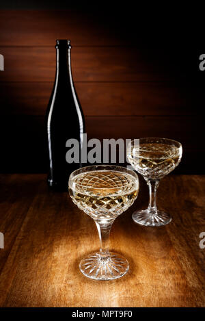 Riflettori puntati su due Champagne bicchieri di cristallo con una bottiglia in background, shot su un antico tavolo di legno alto. Foto Stock